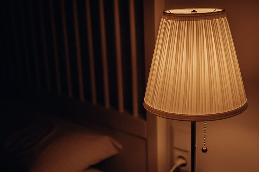 Warm glowing bedside lamp in early morning light - illustrative category image